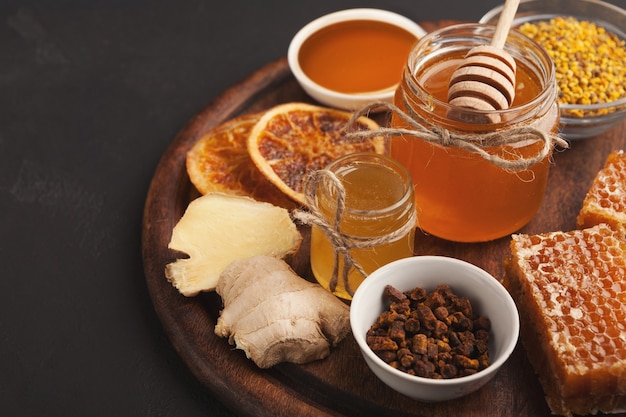 Assortiment de miel, gros plan. Bocal en verre, nids d'abeilles, bol de pollen, noix, gingembre, menthe et oranges sèches. Fond doux, papier peint. Concept de médecine naturelle