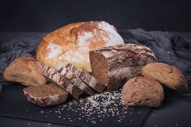 Assortiment de pains cuits au four sur fond sombre. Concept de magasin d'alimentation de boulangerie et d'épicerie.