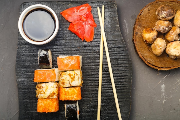 Assortiment de petits pains sur une planche noire faite à la main à côté de bâtonnets de sauce soja et de champignons cuits au four