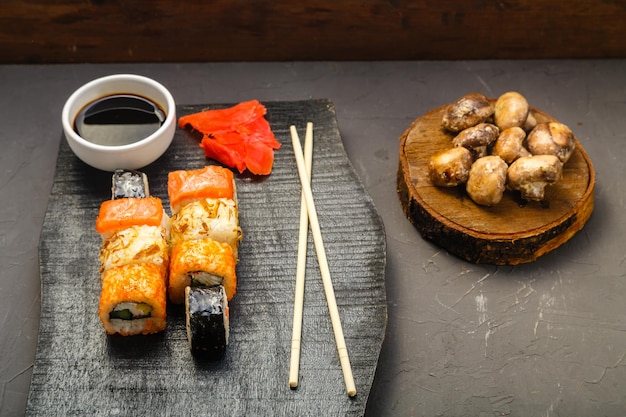 Assortiment de petits pains sur une planche noire faite à la main à côté de bâtons, de sauce soja et de champignons cuits au four sur fond sombre. Photo horizontale