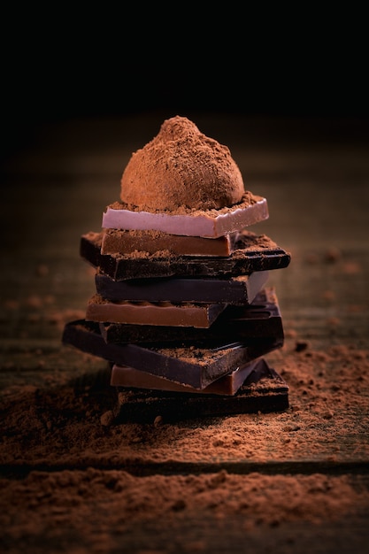 Assortiment de pile de chocolat noir et lait, truffes. Chocolat avec de la poudre de cacao sur une table en bois rustique sombre. Mise au point macro sélective. Bonbons et fond de chocolat.