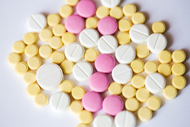 Assortiment de pilules de médecine pharmaceutique. Comprimés jaunes et roses sur fond blanc.