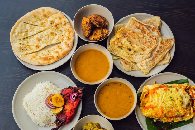 Assortiment de plats indiens sur fond de bois foncé Plats et apéritifs de la cuisine indienne Curry poulet au beurre riz lentilles paneer samosa naan chutney épices Bols et assiettes avec de la nourriture indienne