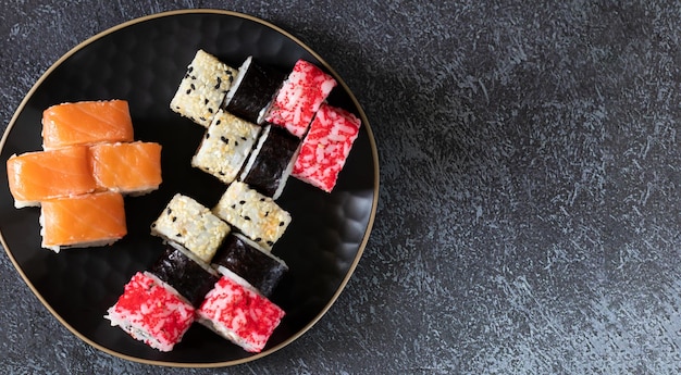 Assortiment de rouleaux de sushi sur une plaque noire sur fond sombre avec un espace de copie sur la droite Vue de dessus mise à plat horizontale