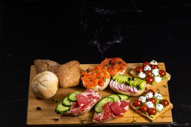 Un assortiment de sandwichs avec du poisson, du fromage, de la viande et des légumes était posé sur la planche et un petit pain.