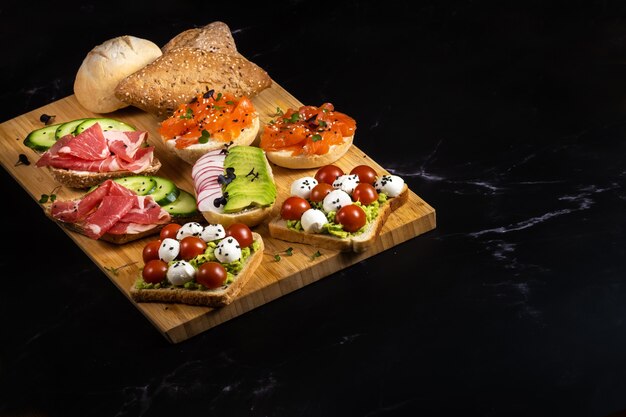 Un assortiment de sandwichs avec du poisson, du fromage, de la viande et des légumes était posé sur la planche et un petit pain.