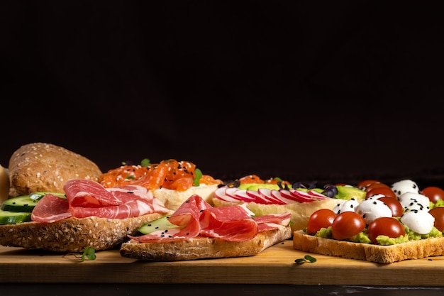 Un assortiment de sandwichs avec du poisson, du fromage, de la viande et des légumes était posé sur la planche et un petit pain.