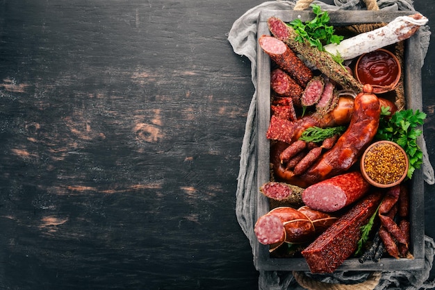 Assortiment de saucisses et de collations dans une boîte en bois Sausage Fuet salami paperoni Sur fond noir Vue de dessus Espace libre pour votre texte