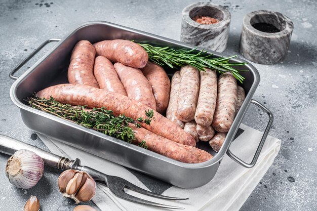 Assortiment de saucisses crues boeuf porc agneau et poulet saucisses de viande hachée dans un plateau de cuisine en acier avec des herbes fond gris vue de dessus