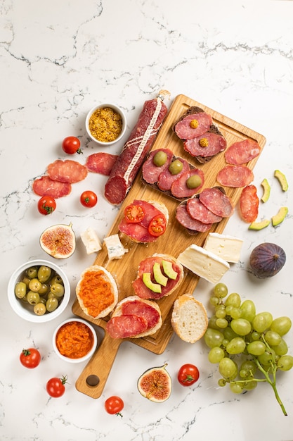 Assortiment de saucisses et fromages, brie de camembert salami, raisins, tranches de baguette, olives, sur fond de pierre blanche. Table d'apéritifs avec des collations antipasti. Fond de marbre blanc. Vue de dessus