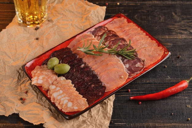 Assortiment de saucisses tranchées sur une plaque rouge. Avec un verre de bière. Sur une table en bois