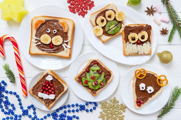 Assortiment de toasts d'animaux drôles avec du chocolat, des fruits frais, des guimauves sur des assiettes, vue de dessus. L'idée d'un menu pour une fête d'enfants. Petit déjeuner créatif, thème de Noël.