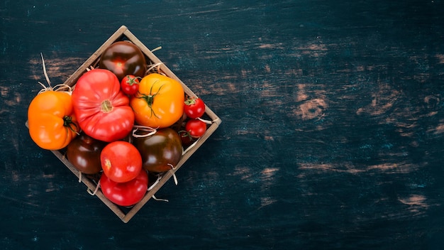 Assortiment de tomates dans une boîte en bois. Légumes frais. Sur un fond en bois noir. Vue de dessus. Copiez l'espace.