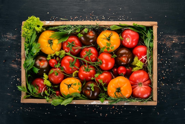 Assortiment de tomates dans une boîte en bois Légumes frais Sur un fond en bois noir Vue de dessus Espace de copie