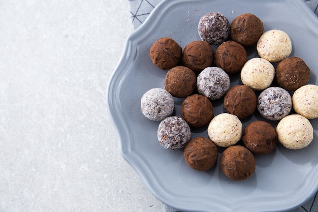 Assortiment de truffes au chocolat avec poudre de cacao, noix de coco et noisettes hachées dans une assiette à dessert