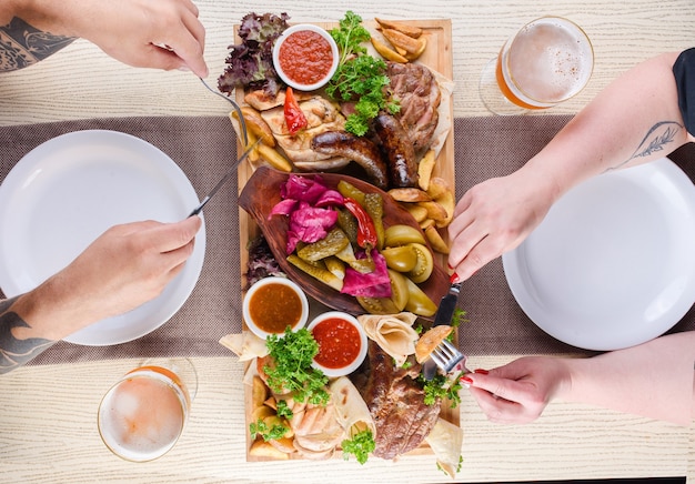 Assortiment de viande frite, pommes de terre, saucisses, cornichons, tomates, poivrons, herbes, lavash sur un plateau en bois sur la table. Vue de dessus.