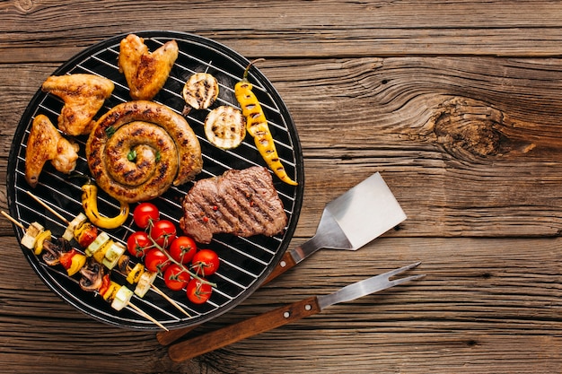Assortiment de viande et de saucisses marinées à griller sur un barbecue sur fond en bois