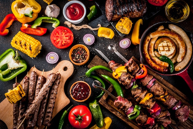 Assortiment de viandes de grillades de grillades variées, bbq party fest - shish kebab, saucisses, filet de viande grillé, légumes frais, sauces, épices, table en béton rouillé foncé, au-dessus de l'espace de copie