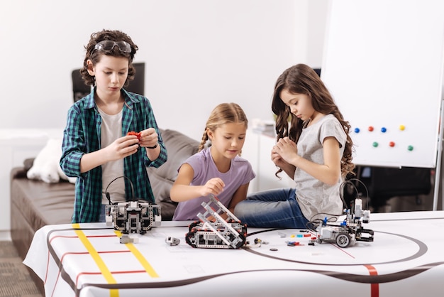 Assumer nos responsabilités. Mignon impliqué des enfants assidus assis dans le laboratoire de robotique et testant des appareils électroniques tout en ayant une leçon de sciences