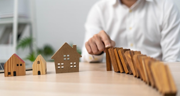 L'assurance avec les mains protège une maison Le domino en bois est sur le point de tomber sur la maison Concept d'assurance habitation ou d'assurance habitation