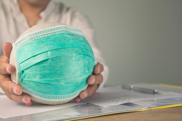 Assurance maladie dans le concept COVID Un homme tient une boule blanche avec un masque médical vert Papier de contrat sur la table L'espace de copie est sur le côté droit de cette photo