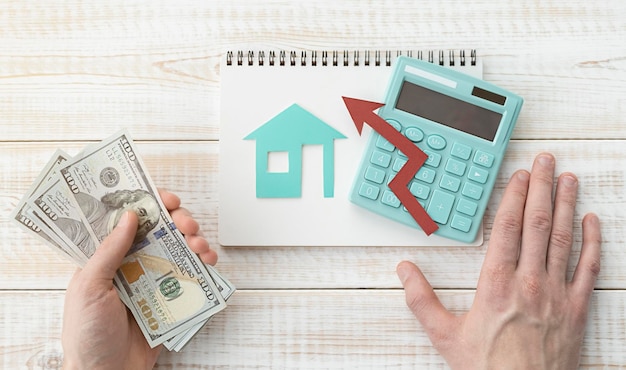 Assurance et protection de l'immobilier Les mains de l'homme tiennent des dollars avec une calculatrice et une figurine d'une maison sur la table