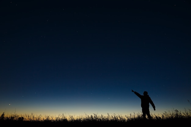 L'astronome pointe sa main la nuit sur le ciel étoilé sur fond d'horizon crépusculaire.