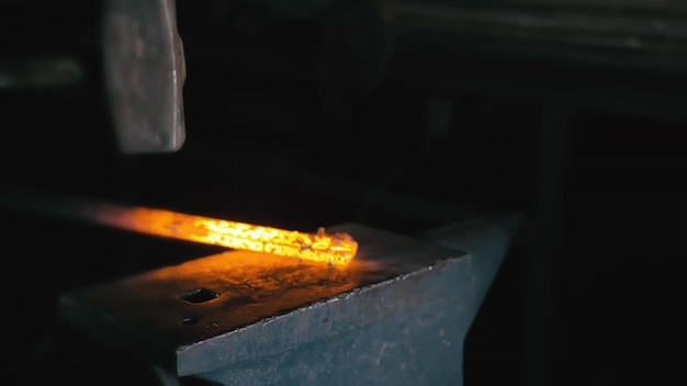 Atelier de forge Smithy production manuelle Mains de forgeron avec un marteau frappé sur du métal chaud brillant sur l'enclume le processus de forgeage Le forgeron fabrique des produits en fer pour la fabrication d'un poêle à bois