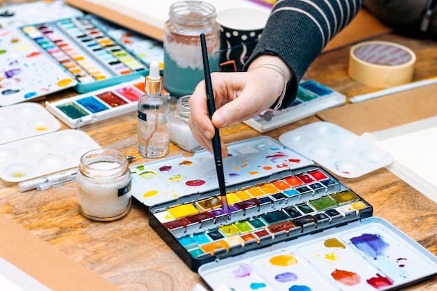 Atelier de peinture à l'aquarelle Gros plan d'une main de jeune femme mélangeant les couleurs avec un pinceau