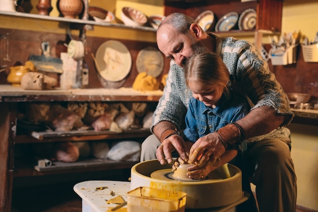 Photo atelier de poterie. grand-père enseigne la poterie à sa petite-fille. modelage d'argile