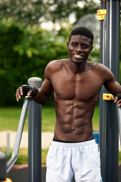 Un athlète afro-américain souriant effectue des exercices abdominaux, un athlète en excellente forme physique fait des exercices abdominaux dans la rue sur le terrain de sport.
