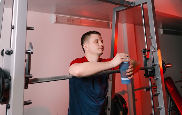 L'athlète après l'entraînement se tient près de la barre et tient un shaker avec une boisson protéinée. gym moderne de mode de vie sain.