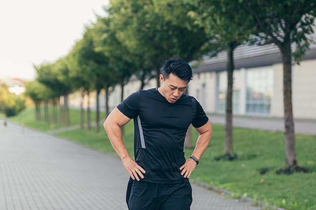 Athlète asiatique masculin, fatigué après un jogging matinal, court dans le parc près du stade
