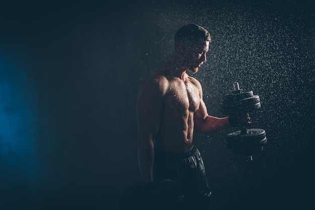 Un athlète blond masculin soulève des haltères avec la main sur une photo de studio de biceps avec des gouttes de pluie