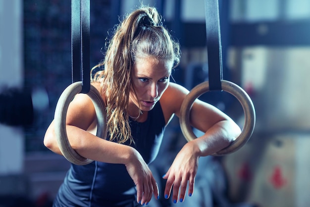 Une athlète fatiguée faisant de l'exercice avec des anneaux de gymnastique au gymnase