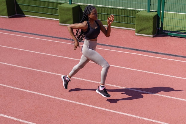 Athlète féminine africaine courant sur une piste de course sportive féminine noire entraînant le jogging sur le sprint du stade