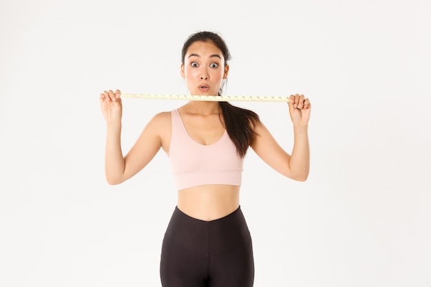 Athlète féminine asiatique impressionnée et heureuse montrant un ruban à mesurer après ma taille et perdre du poids avec un programme d'entraînement, aller au gymnase.