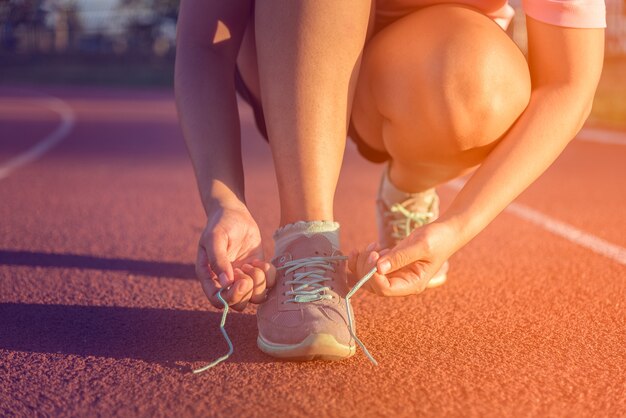 Athlète féminine attachant des lacets pour faire du jogging, coucher de soleil