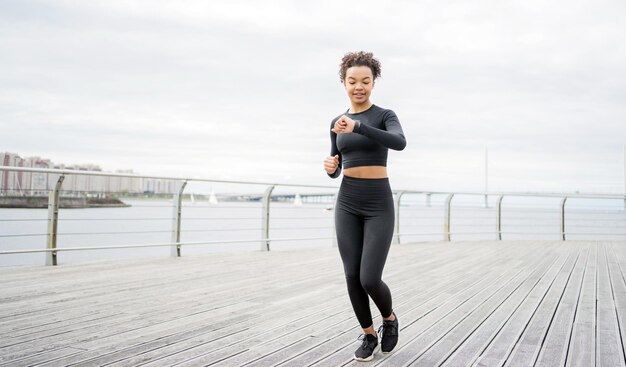 L'athlète féminine en cours d'exécution fait des exercices de fitness cardio actifs utilise une montre de fitness et un tracker pour mesurer son pouls