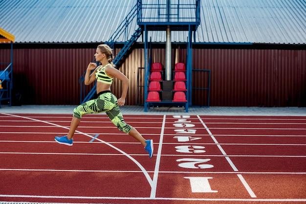 Une athlète féminine court le long du fond de sport sur tapis roulant