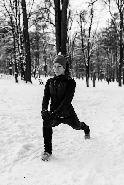 Athlète féminine faisant de l'exercice dans le parc le jour de l'hiver, écoutant de la musique et faisant de l'exercice