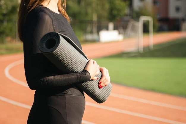 Une athlète féminine de race blanche se tient au stade sur une piste de course avec un tapis de yoga prêt pour l'entraînement