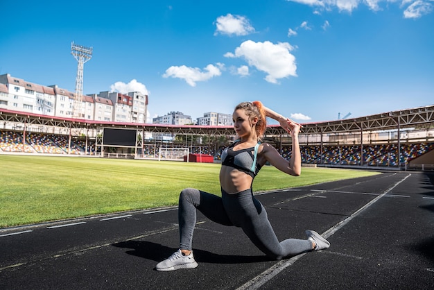 Athlète féminine sexy s'entraînant sur le stade en plein air, exercice d'étirement pour un mode de vie actif