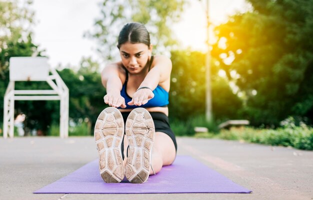 Athlète femme assise faisant des étirements de jambes dans un parc Athlète fille assise sur un tapis étirant ses jambes dans un parc Fille sportive étirant ses jambes assise sur un tapis dans un parc