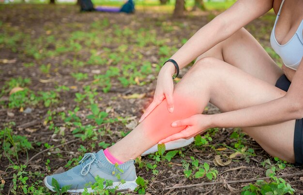 Athlète fille assise sur l'herbe avec douleur à la jambe Fille sportive endolorie assise sur l'herbe se frottant la jambe Athlète en plein air femme concept de douleurs aux jambes Athlète femme se frottant la jambe assise sur l'herbe