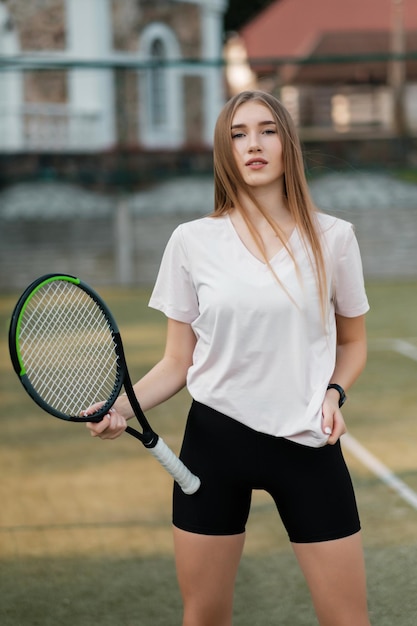 Athlète de fille dans un t-shirt blanc et un short serré noir avec une raquette sur le court de tennis Concept de mode et de sport