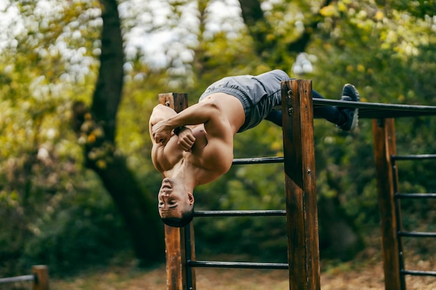 Un athlète fort sans chemise fait des exercices pour les abdominaux dans une salle de sport en plein air dans la nature.