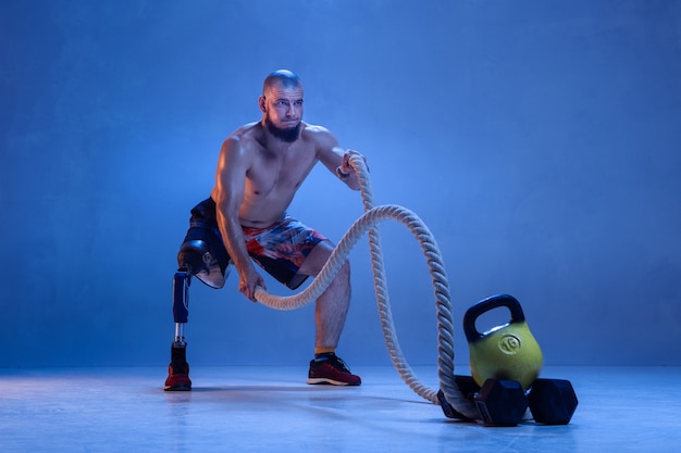 Athlète handicapé ou amputé isolé sur mur bleu. Sportif masculin professionnel avec formation de prothèse de jambe avec des cordes en néon. Sport handicapé et dépassement, concept de bien-être.