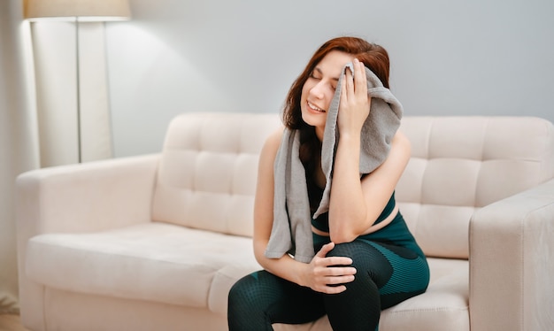 Une athlète heureuse se repose et essuie sa sueur avec une serviette après un entraînement intensif à la maison pour nous...