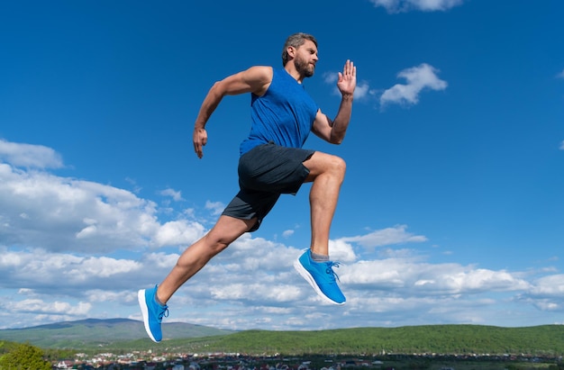 Athlète homme énergique avec corps musclé courir en tenue de sport en plein air sur fond de ciel, jogging